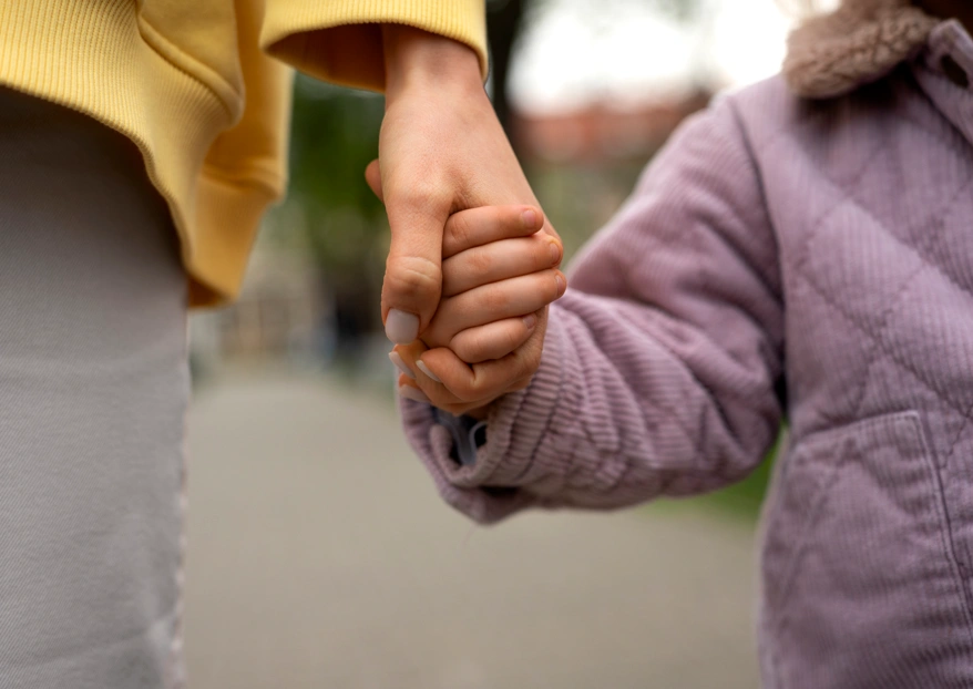 Close-up of a parent holding a young child's hand, symbolizing the financial stability and care secured with the help of an Orange County child and spousal support attorney.
