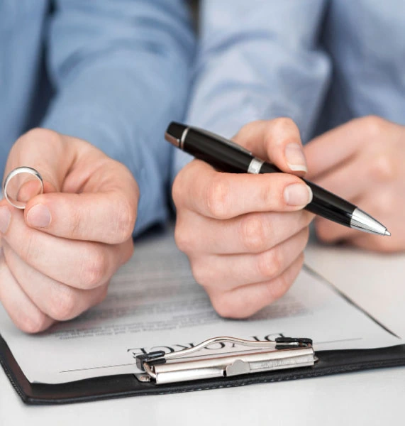 Close-up of hands signing a divorce document and holding a wedding ring, representing high-asset divorce cases in Orange County.