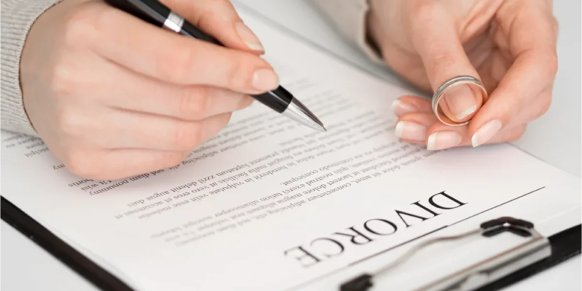 A person holding a wedding ring and signing legal documents, illustrating the first steps of how to file for divorce in Orange County.