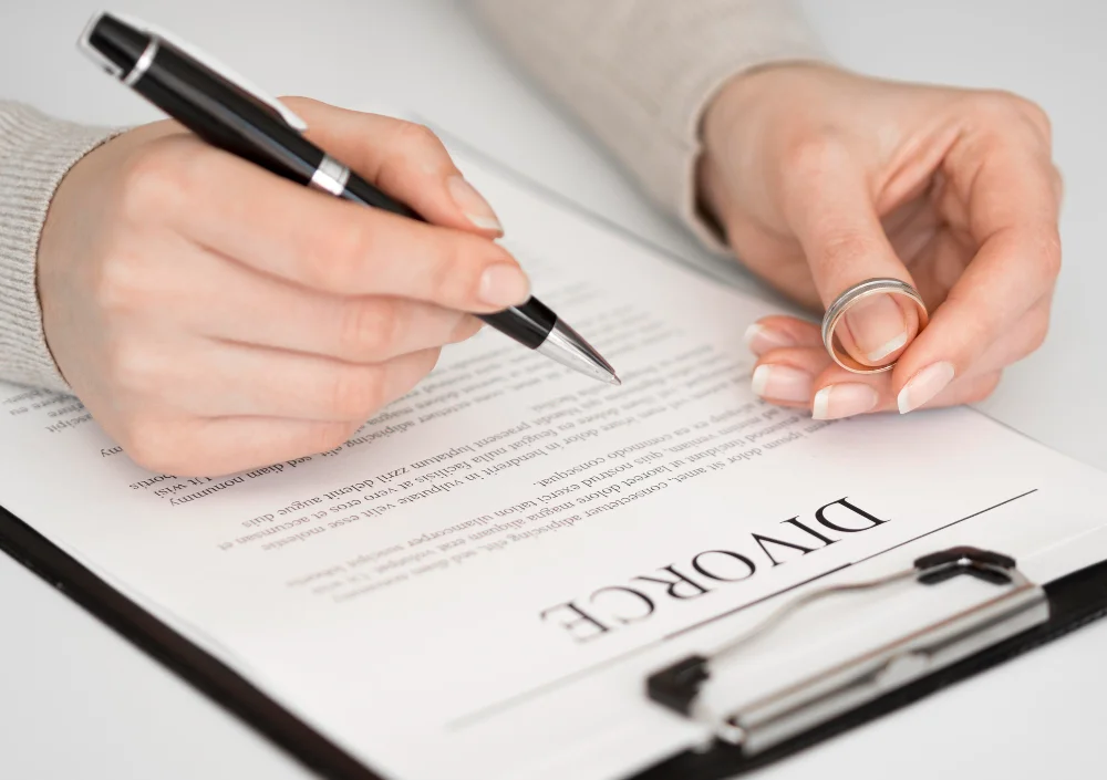 A person holding a wedding ring and signing legal documents, illustrating the first steps of how to file for divorce in Orange County.