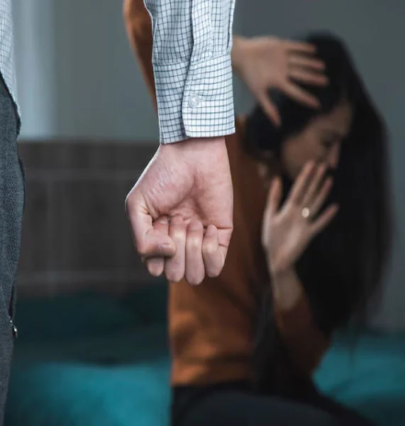 A woman shielding herself from a man's clenched fist, symbolizing domestic abuse situations where an Orange County domestic violence lawyer can provide legal help.